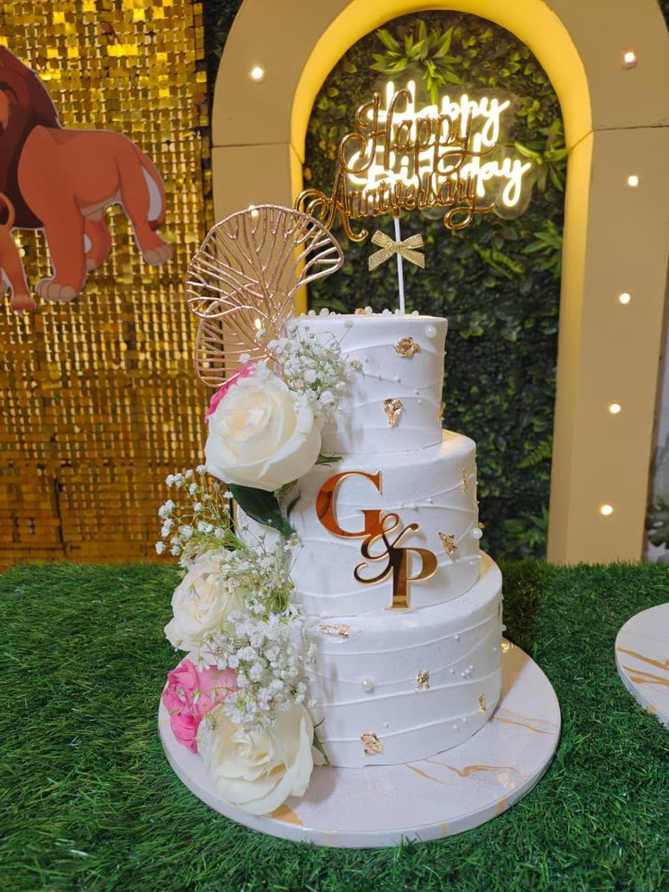 Three-tier white anniversary cake with a gold monogram and fresh roses