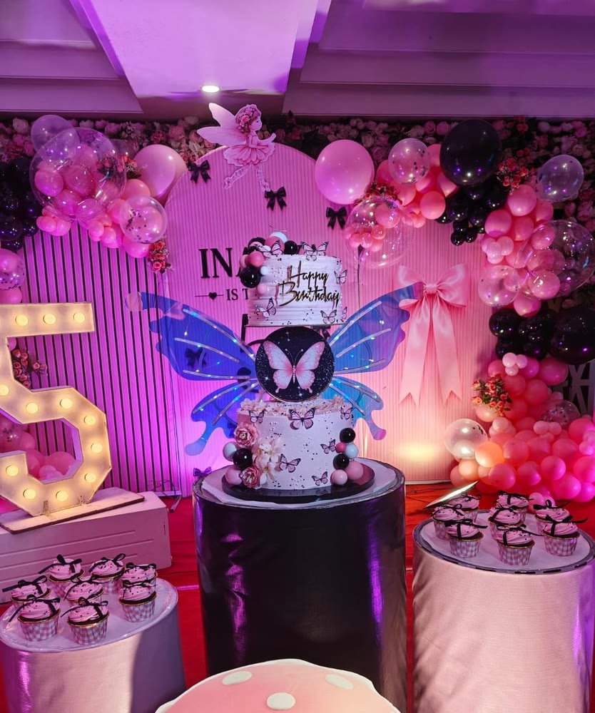 Two-tier butterfly birthday cake in pink and black, with matching cupcakes