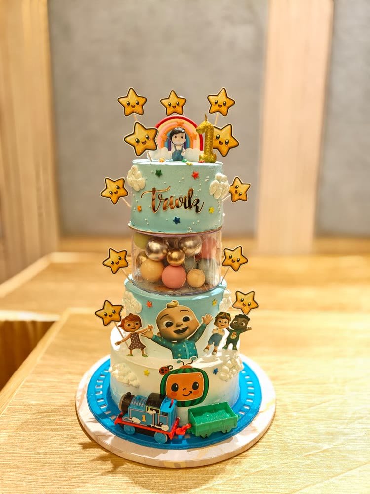 Three-tier first-birthday cake with stars, a ball-filled tier and a toy train