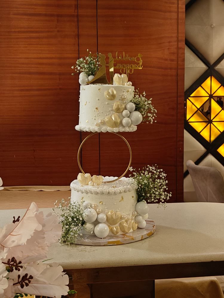 Floating two-tier engagement cake on a gold hoop with white spheres and baby’s breath
