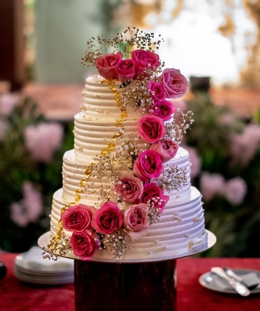 Four-tier ribbed white wedding cake with a cascade of pink roses and a gold drip