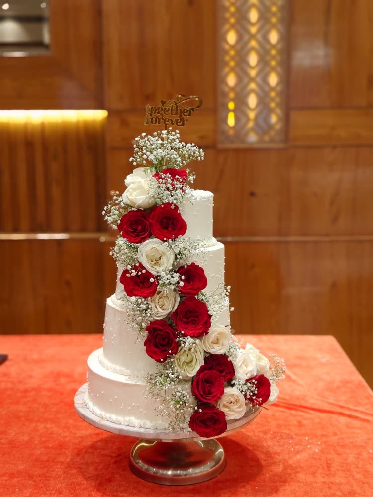 Four-tier white wedding cake with a cascade of red and white roses